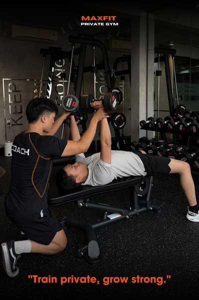 A clean, professional 2:3 vertical ad showing a personal trainer spotting a client during a dumbbell chest press in a private gym setting.